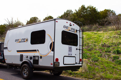 This white Geo Pro travel trailer RV rental is parked on a road next to green hills, with a "Rent Me" sign visible on its rear.