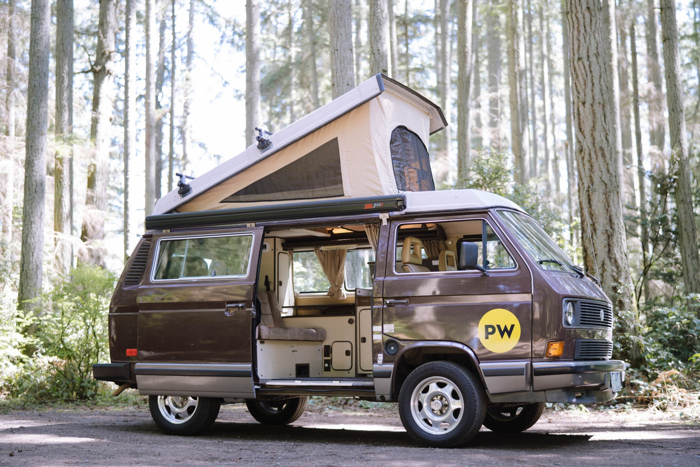  ready for adventure in a sunny forest. Perfect RV rental.|A brown VW pop-top camper van — photo 2