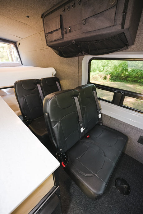 RV rental interior: black passenger seats, overhead storage with pockets, and a rear bed. Ready for adventure!