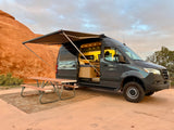 Modern rv rental camper van with extended awning & inviting interior, parked with a picnic table by red rock formations.