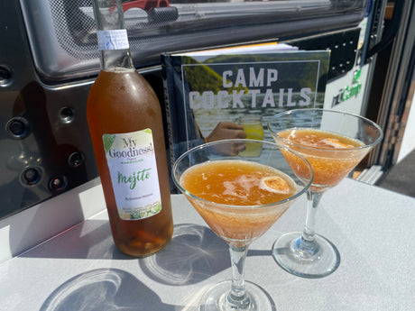 Mojito kombucha cocktails and a "Camp Cocktails" book next to an RV rental, ready for an outdoor adventure.
