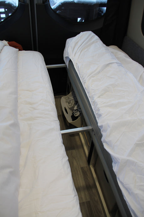 Two beds with white bedding in an RV rental, showcasing efficient interior space and accessible storage.