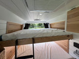 Inside a comfortable RV rental: modern bunk beds with light wood accents and a tranquil park view from the window.