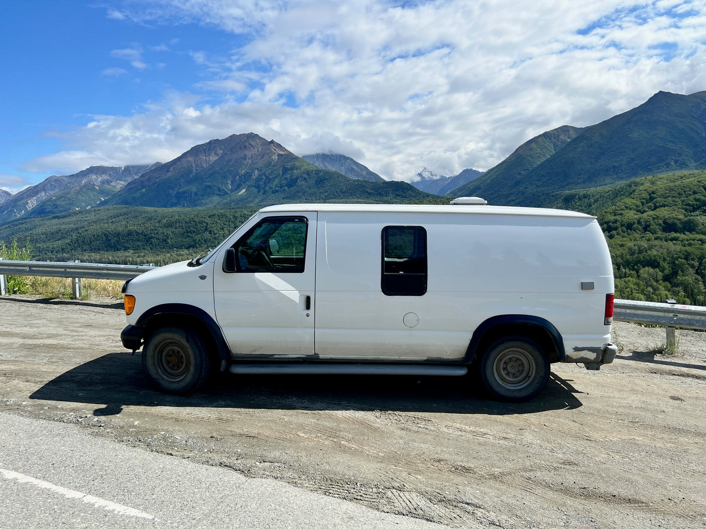White camper van parked roadside by majestic mountains. An RV rental ready for your next scenic adventure!