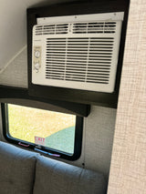 Compact Frigidaire AC and emergency exit window in an RV rental, ensuring cool comfort and safety for your trip.