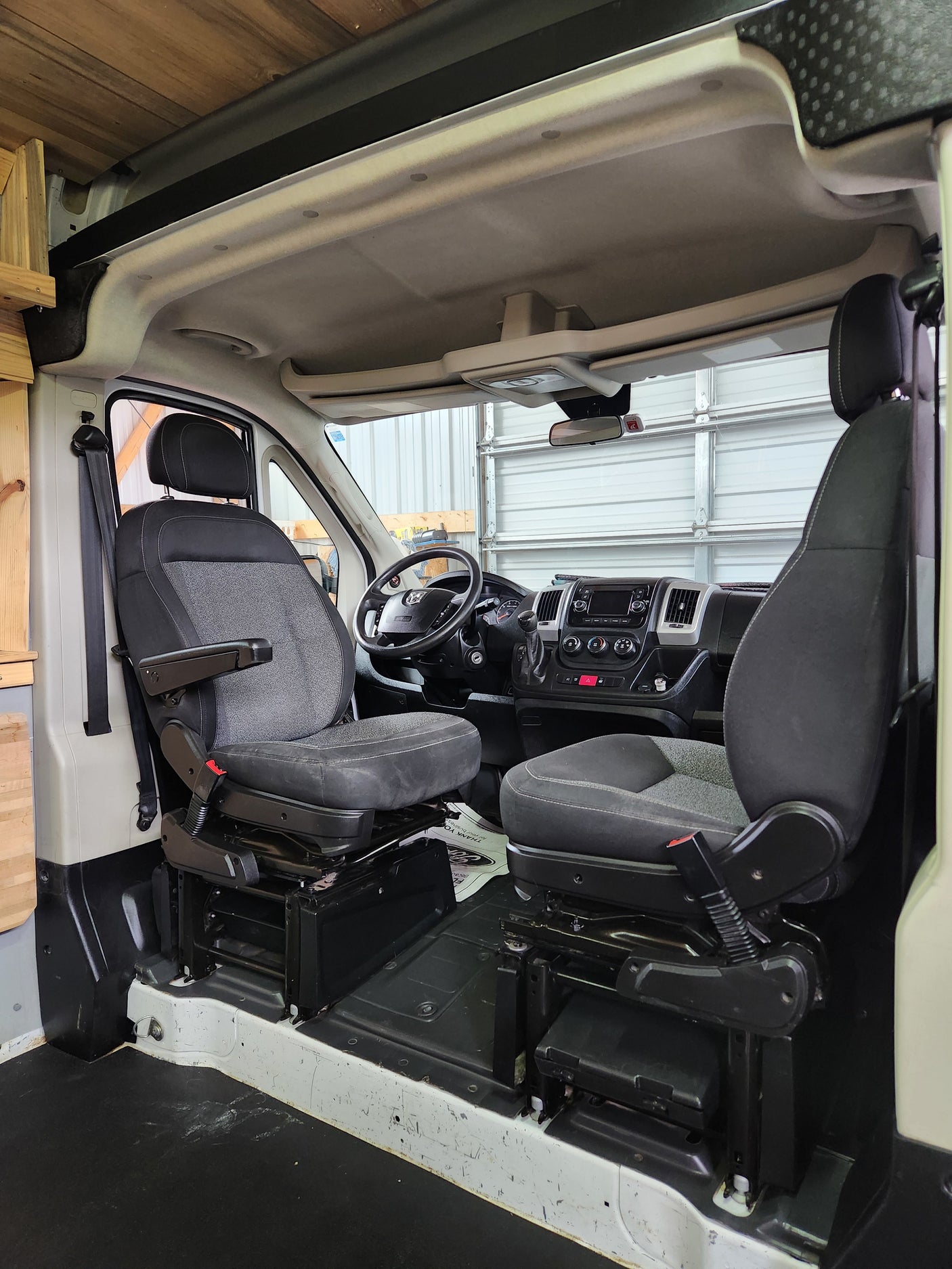 Inside an RV rental conversion van: front cabin with gray driver and passenger seats, dashboard, and wooden ceiling details.