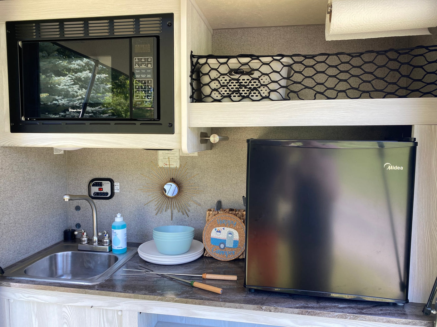 Inside an RV rental, a compact kitchenette features a microwave, sink, and refrigerator, perfect for mobile living and camping. — photo 4