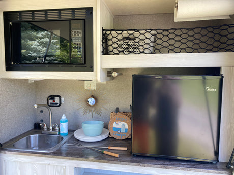 Inside an RV rental, a compact kitchenette features a microwave, sink, and refrigerator, perfect for mobile living and camping.
