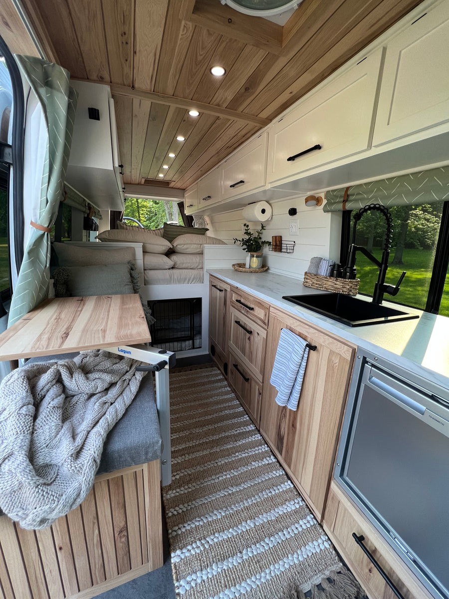 Inside a stylish rv rental: natural wood and white tones create a cozy, compact living space with kitchen, seating & pet nook.