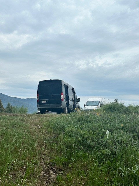 Two rv rental vans on a grassy hill overlooking mountains under a cloudy sky, ready for camping and adventure.