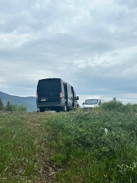 Two rv rental vans on a grassy hill overlooking mountains under a cloudy sky, ready for camping and adventure.