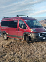 Red Pleasure Way rv rental van (Ram ProMaster) with roof rack, parked in a dry field under a blue sky.