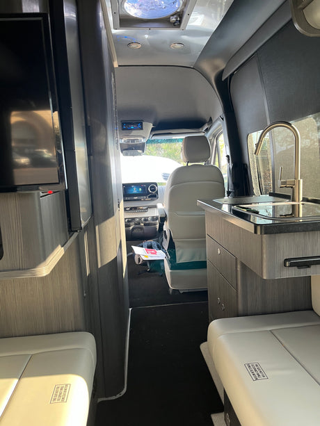 Inside a modern RV rental: looking forward at the kitchen, seating, & driver's cabin. Perfect for compact travel.