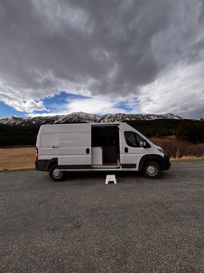 White RV rental camper van with open side door, step stool, parked by snowy mountains under a cloudy sky. — photo 4