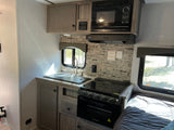 RV rental interior: A compact kitchen with sink, stove, microwave, and an adjacent bed for comfortable travel.