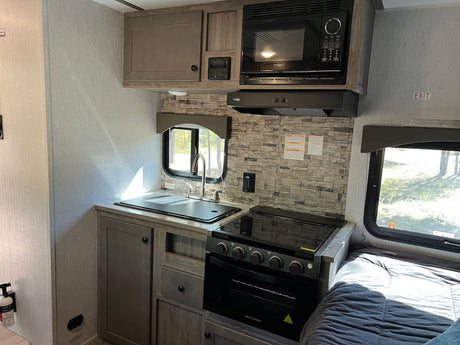 RV rental interior: A compact kitchen with sink, stove, microwave, and an adjacent bed for comfortable travel.