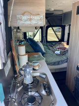 Cozy RV rental interior with kitchen, bed, and "Find Paradise" sign, ready for your next road adventure.