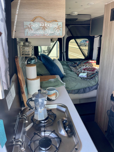 Cozy RV rental interior with kitchen, bed, and "Find Paradise" sign, ready for your next road adventure.