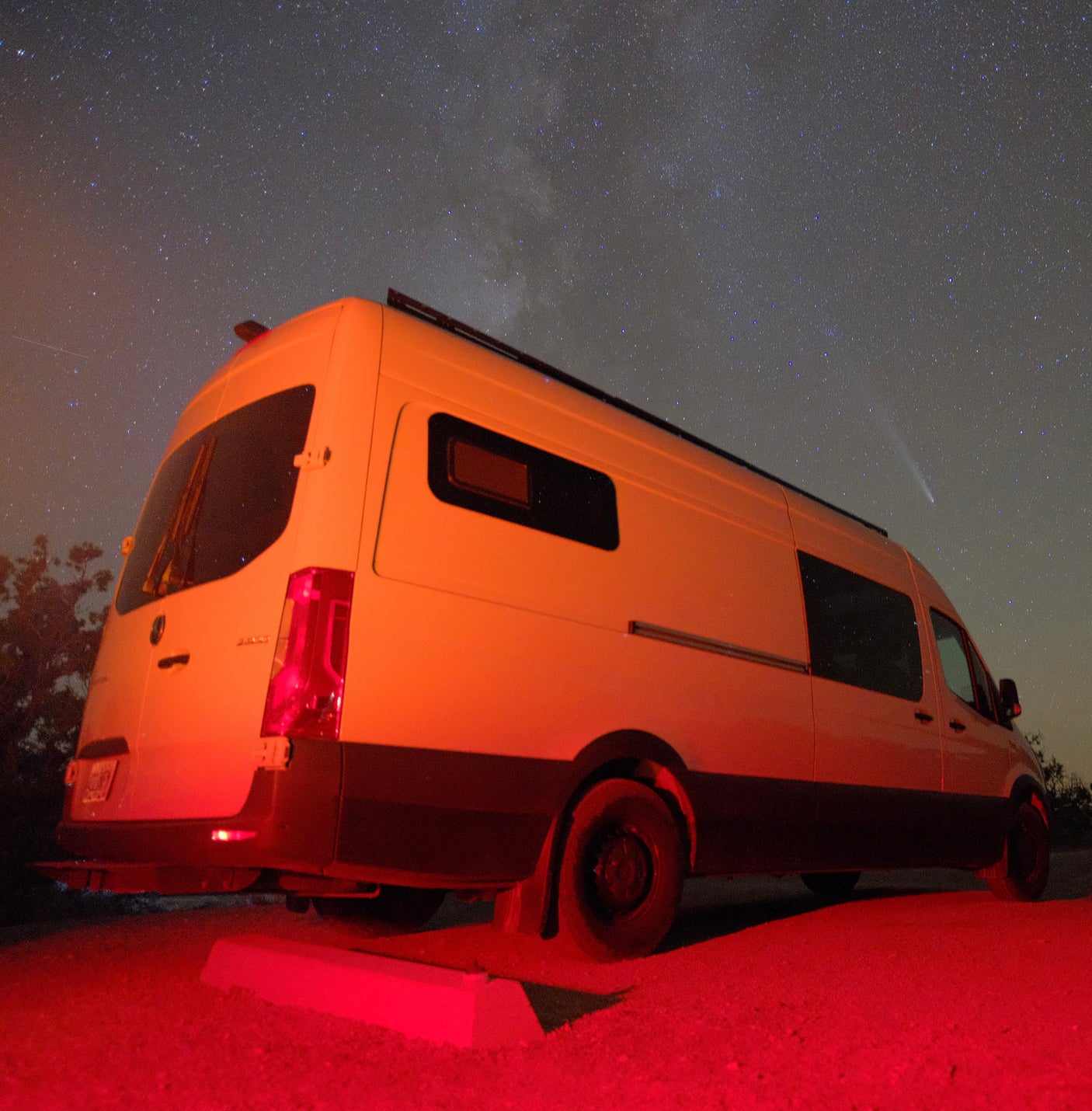 RV rental van bathed in red light under a starry sky with the Milky Way and a bright comet.
