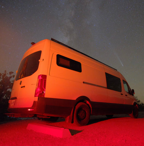 RV rental van bathed in red light under a starry sky with the Milky Way and a bright comet.