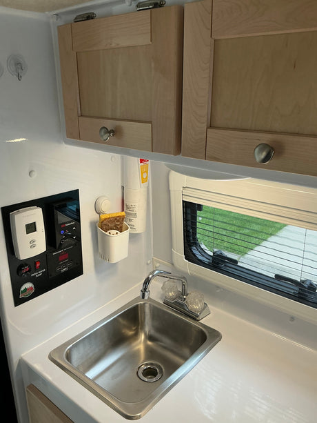 RV rental kitchenette featuring a stainless steel sink, wood cabinets, and system controls for tank levels and temperature.