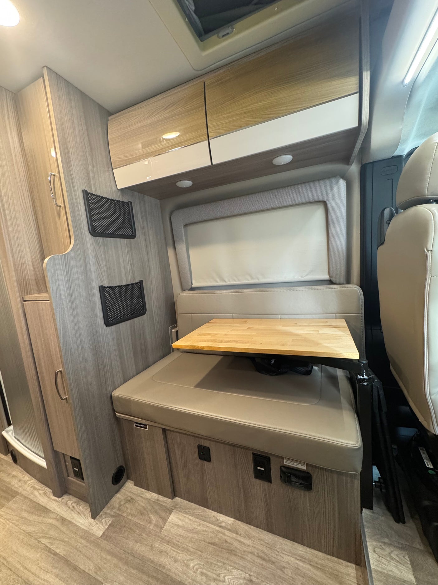Inside this RV rental, a compact dinette area offers cushioned seating, an adjustable wooden table, and overhead storage cabinets.