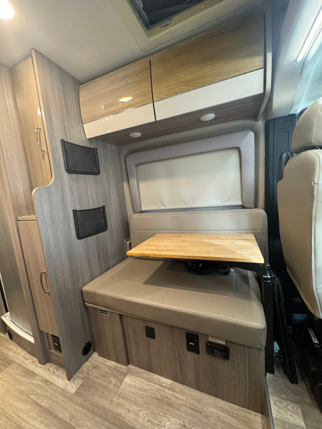 Inside this RV rental, a compact dinette area offers cushioned seating, an adjustable wooden table, and overhead storage cabinets.