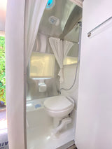 Explore the compact and efficient bathroom setup in this RV rental, with a toilet, shower, and bright interior.