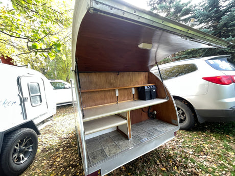Open outdoor kitchen of an rv rental teardrop camper, featuring organized shelves, outlets, and battery power for camping.