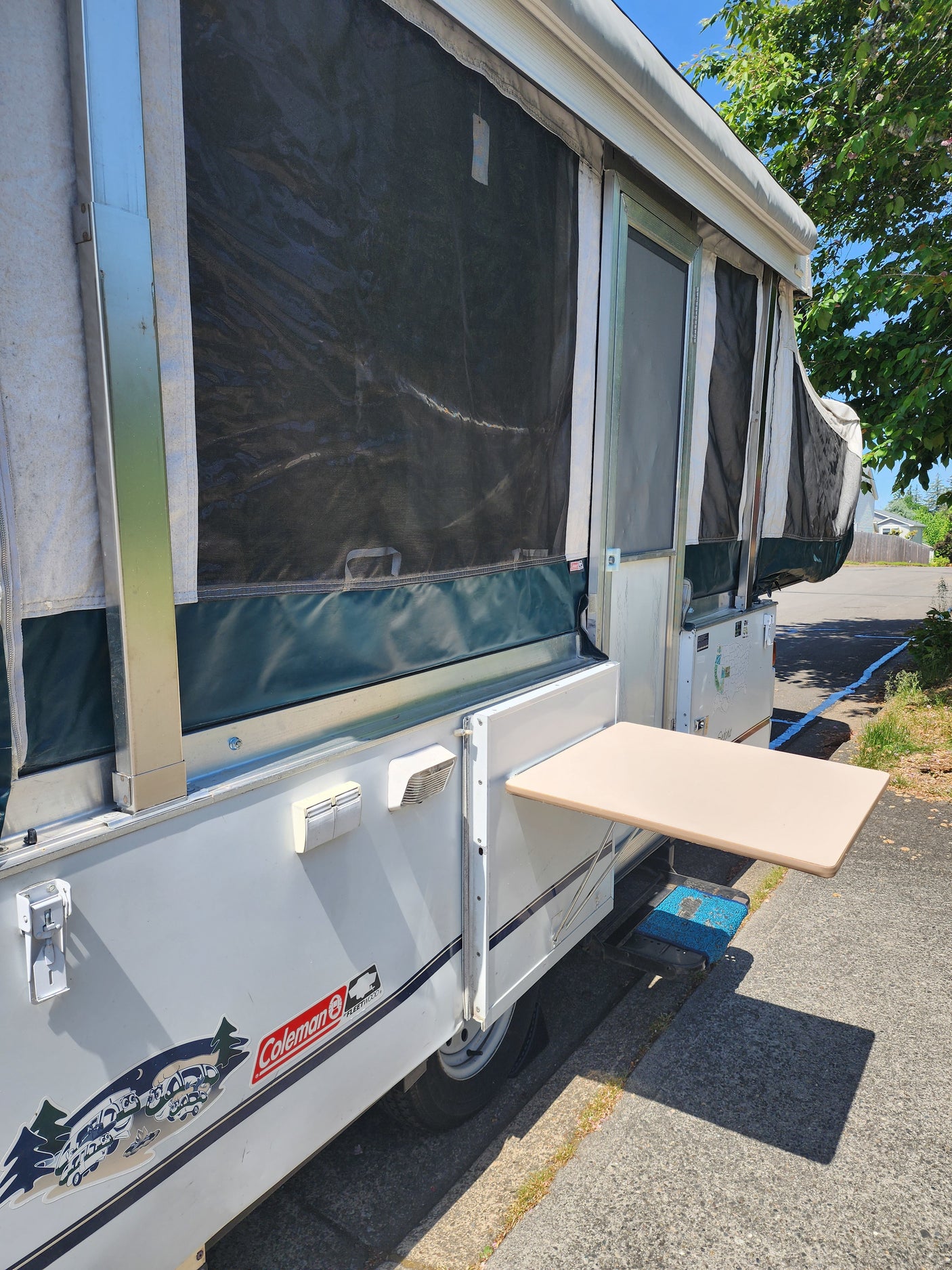 A white Coleman pop-up RV rental with an attached outdoor table, ready for adventures.