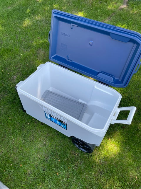 Open white Igloo wheeled cooler on green grass, blue lid beside it, showing gray tray inside. Ideal for your RV rental.