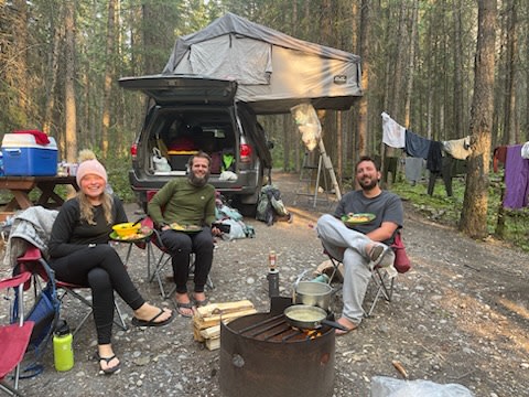  offering a unique RV rental experience for outdoor adventures.|Three smiling campers enjoy a campfire meal at their forest RV rental campsite — photo 7