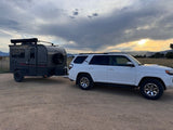 Explore with an RV rental! White SUV tows a gray off-road camper trailer. Ideal for overland adventures at sunset.