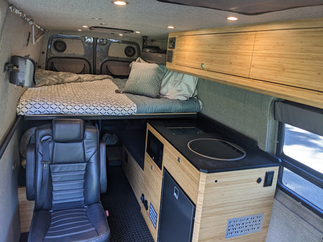 Inside a sleek RV rental: a comfy bed, functional kitchen with microwave & fridge, and plush seating for mobile adventures.