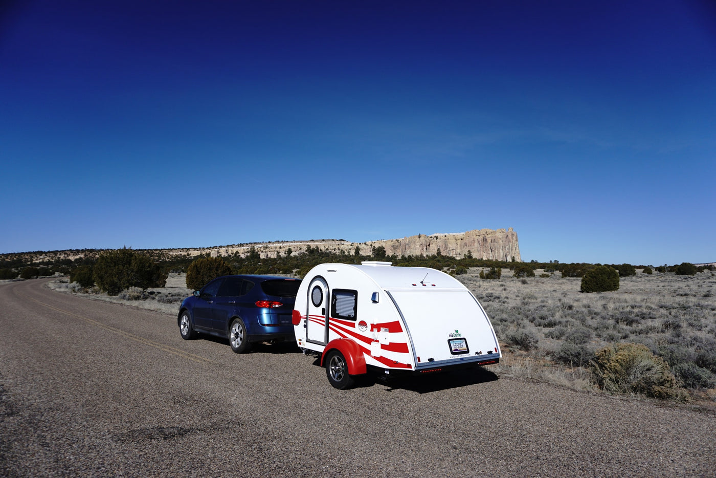 Blue SUV with RV rental teardrop camper parked on a desert road under clear blue skies, with rock formations in background. — photo 7