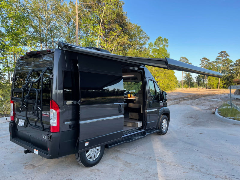 This black camper van, perfect for rv rental, features an extended awning & bike rack, parked outdoors. — photo 18