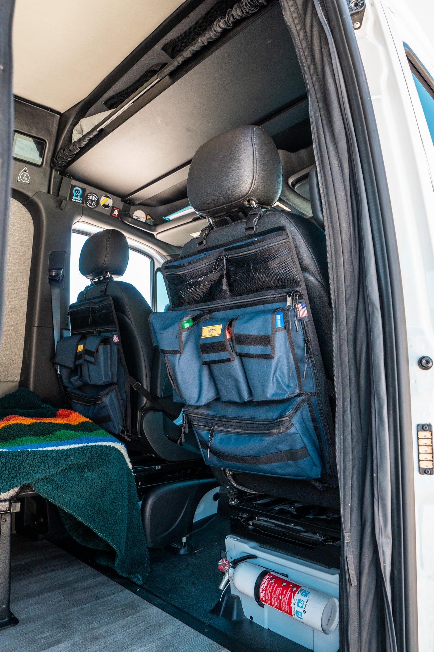 RV rental interior: practical seat-back organizers, fire extinguisher, and cozy blanket for efficient, safe travels.