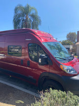 A vibrant red camper van, perfect as an RV rental, is parked under a clear sky on a sunny day.