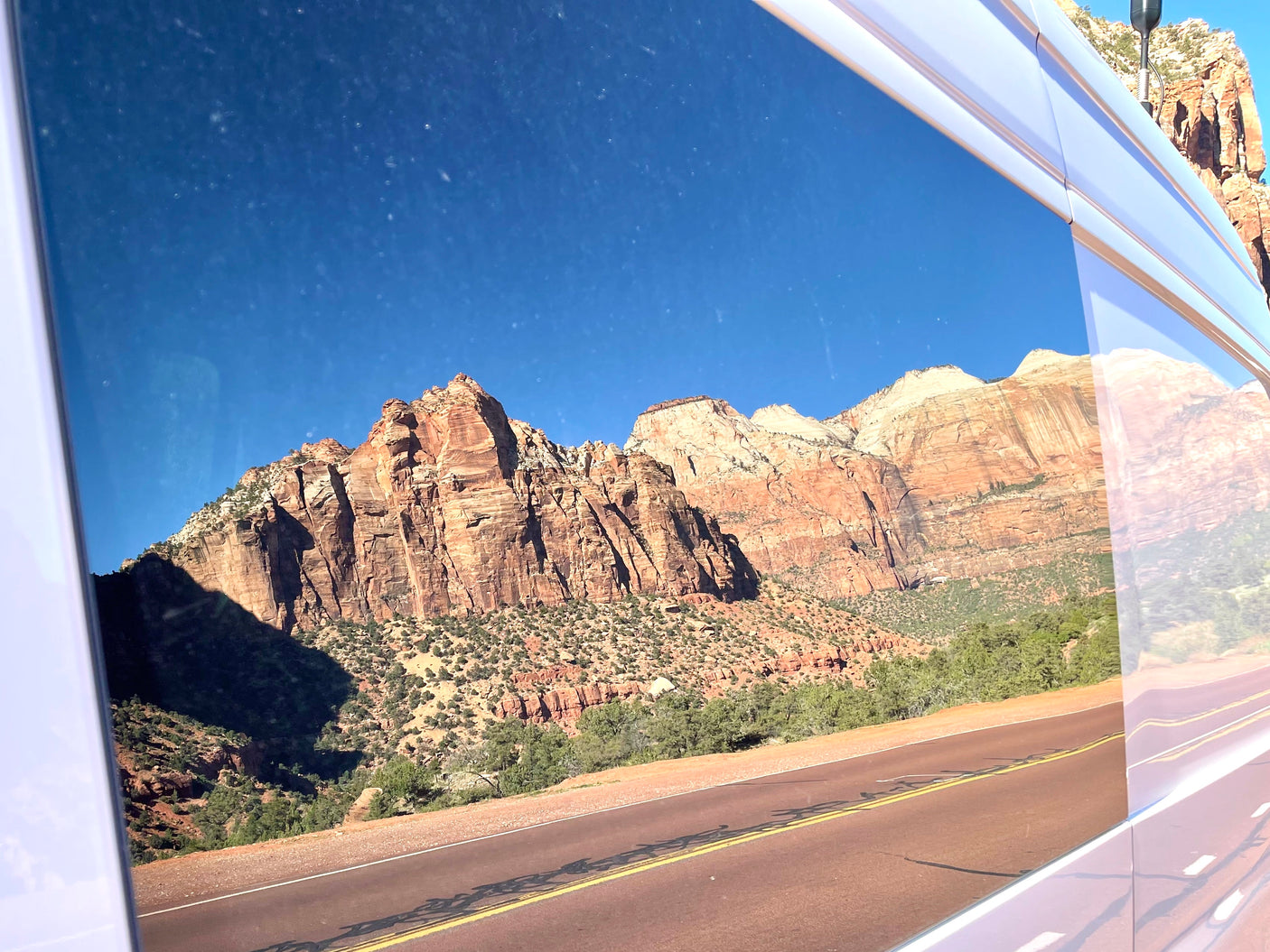 Red rock mountains of Zion National Park vividly reflected in an RV rental window, showcasing a beautiful scenic drive.