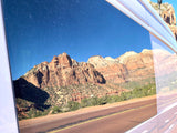 Red rock mountains of Zion National Park vividly reflected in an RV rental window, showcasing a beautiful scenic drive.