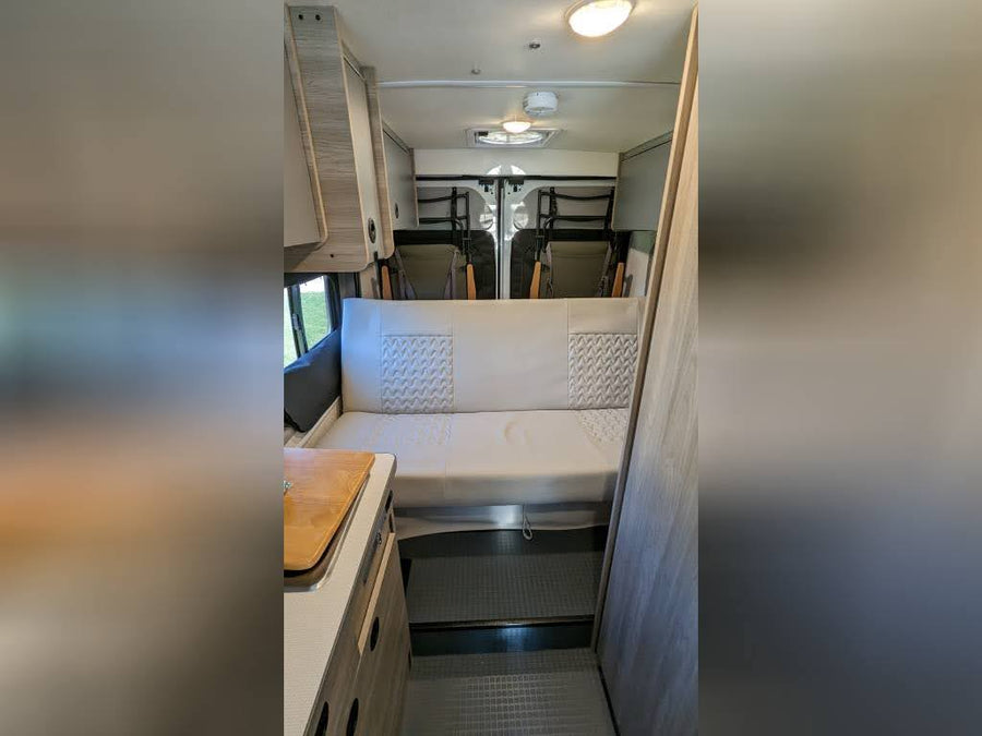  offering a view outside for your adventure.|An RV rental emerges from a natural rock tunnel. Its bright headlights illuminate the rugged passage and a mountain view.|Bright day