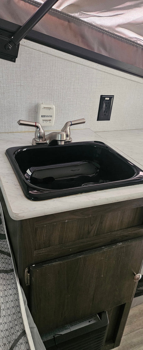 This RV rental features a compact kitchen counter with a black sink, brushed nickel faucet, and a Suburban thermostat.
