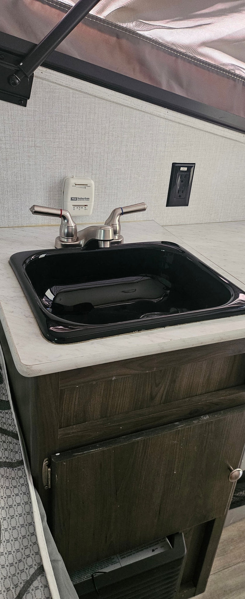 This RV rental features a compact kitchen counter with a black sink, brushed nickel faucet, and a Suburban thermostat. — photo 13