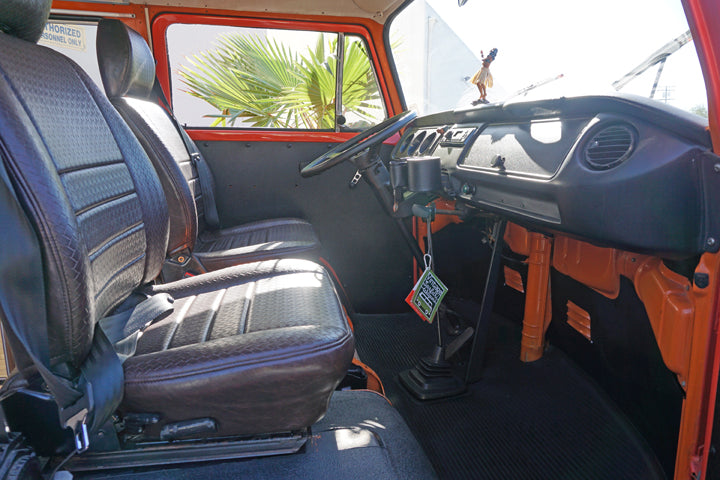 Interior of a vintage RV rental: front seats, dash, and manual shift in the driver's cabin. Ready for adventure!