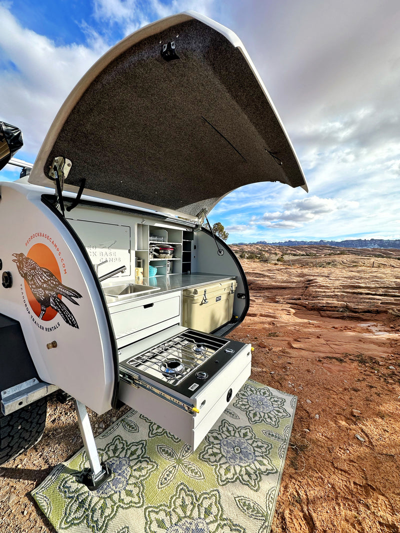 Teardrop camper RV rental outdoor kitchen with sink, stove, and cooler, set up in a red rock desert. — photo 11