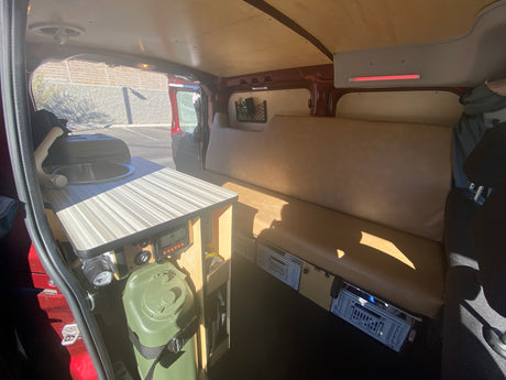 Functional camper van interior: Features a compact kitchen with sink, long bench seat, and under-seat storage, ideal for an RV rental.