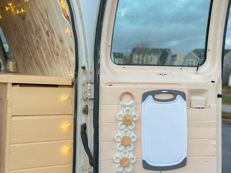 RV rental interior: organized storage with decorative lights, macrame art, and a practical cutting board mounted on the back door.