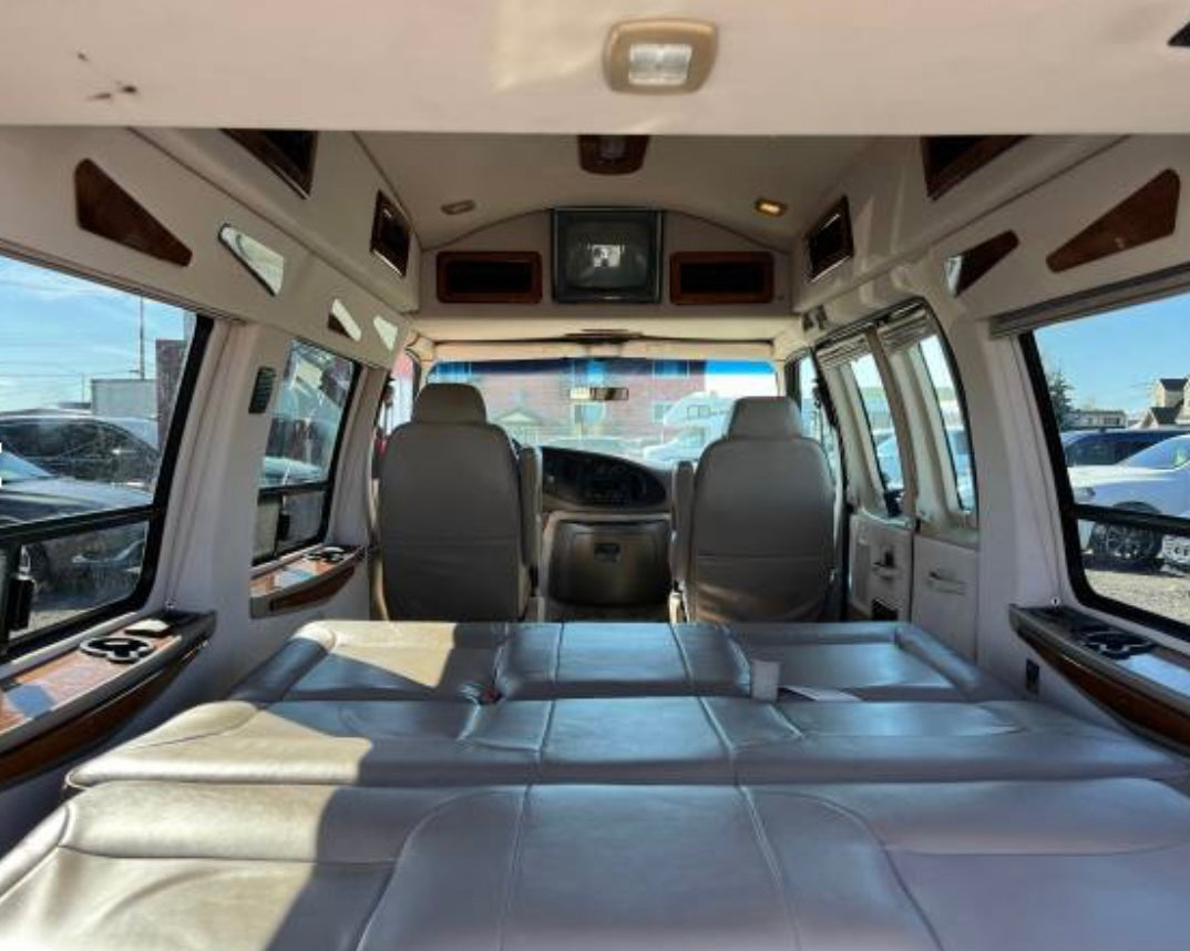 This RV rental's spacious interior features light leather seats that convert to a bed, viewed from the rear.