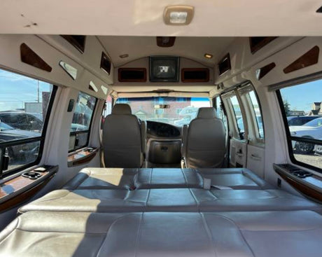 This RV rental's spacious interior features light leather seats that convert to a bed, viewed from the rear.