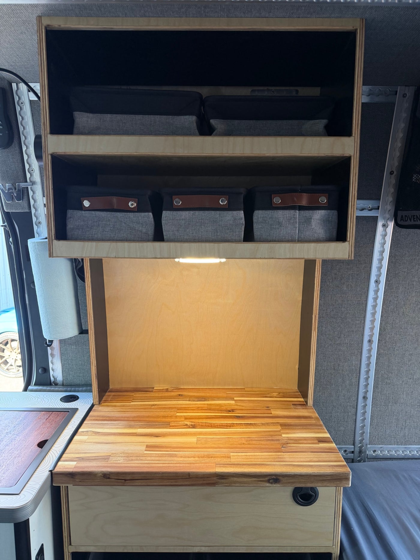 RV rental interior: Organized wooden cabinets, bright countertop lighting, and fabric storage bins in a compact camper kitchen. — photo 12